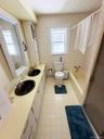 Dual vanity with black basins, built-in storage cabinetry, window, and bath/shower combination