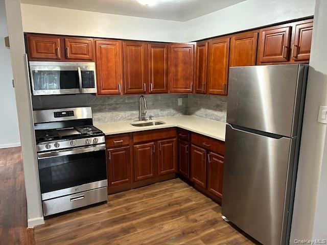 Kitchen with appliances with stainless steel finishes, backsplash, dark wood-style floors, light stone counters, and dark brown cabinets