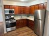 Kitchen with appliances with stainless steel finishes, backsplash, dark wood-style floors, light stone counters, and dark brown cabinets