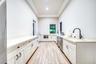 Expansive kitchen featuring wood-finish flooring, white cabinetry with dark hardware, light-toned countertops, a stainless steel dishwasher, and a dee