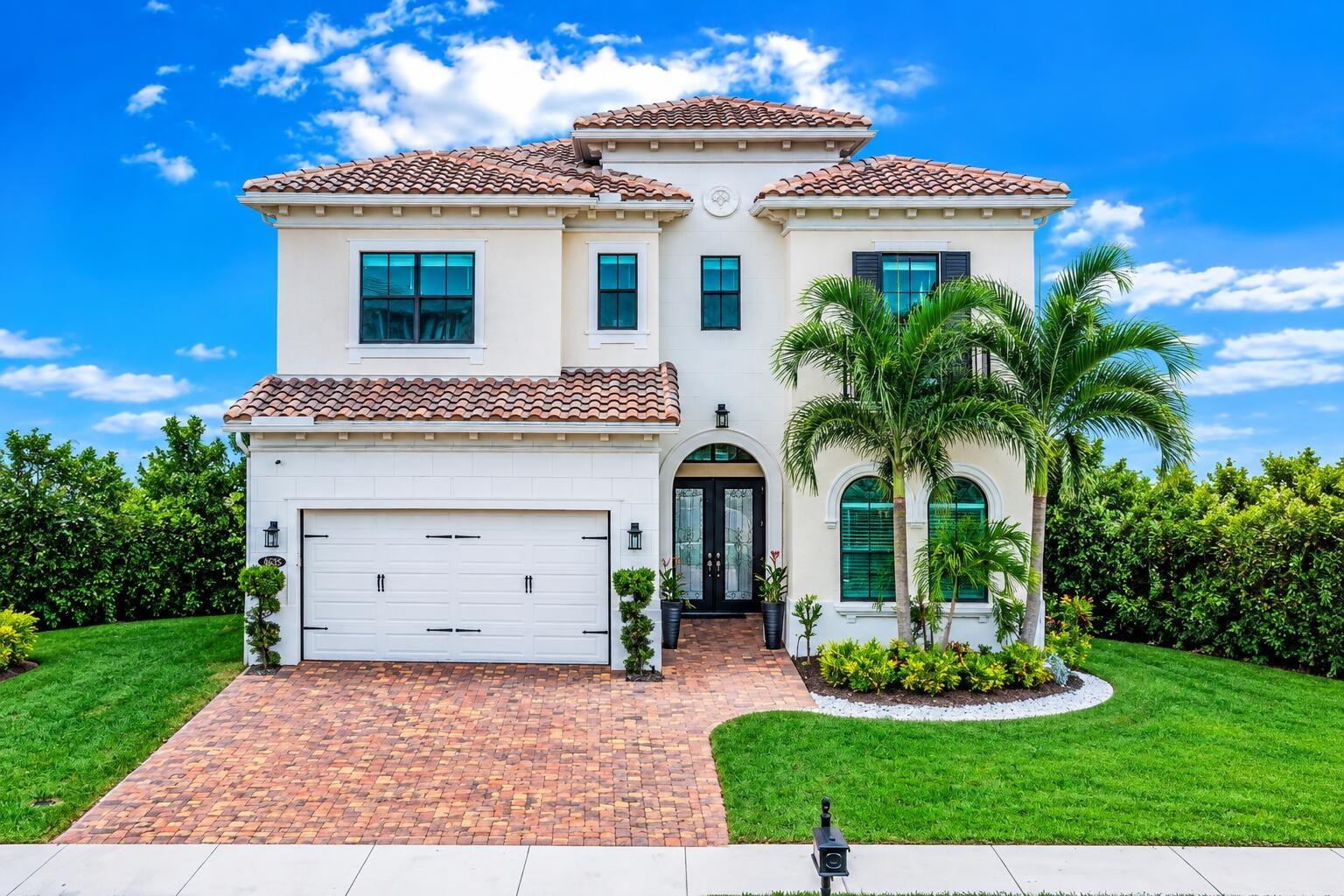 Stucco exterior with a tile roof, brick paver driveway, arched entry, double front doors, and manicured landscaping
