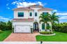 Stucco exterior with a tile roof, brick paver driveway, arched entry, double front doors, and manicured landscaping