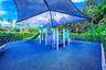 Recreational area featuring a shade structure, play equipment with slides, a blue cushioned ground surface, and perimeter fencing