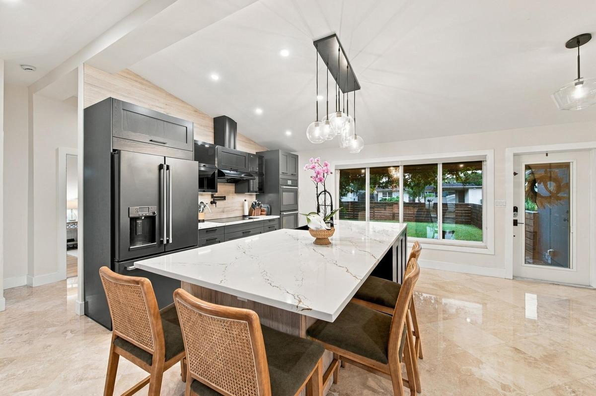 Expansive kitchen island with a white veined countertop, dark cabinetry, stainless steel appliances, and recessed lighting