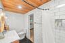 White subway tile walls, wood-finish ceiling, black hexagonal floor tiles, white vanity with integrated sink, and clear glass globe light fixtures