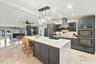 Kitchen featuring a waterfall-edge island with seating, a pendant light fixture, dark cabinetry, and dual built-in ovens