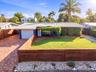 Metal roof, wood privacy fencing, brick paver driveway, manicured lawn, and lush landscaping