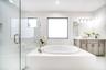 Freestanding soaking tub with brass-finish fixtures, dual sink vanity with stone countertop, glass-enclosed shower with tiled walls, and large windows