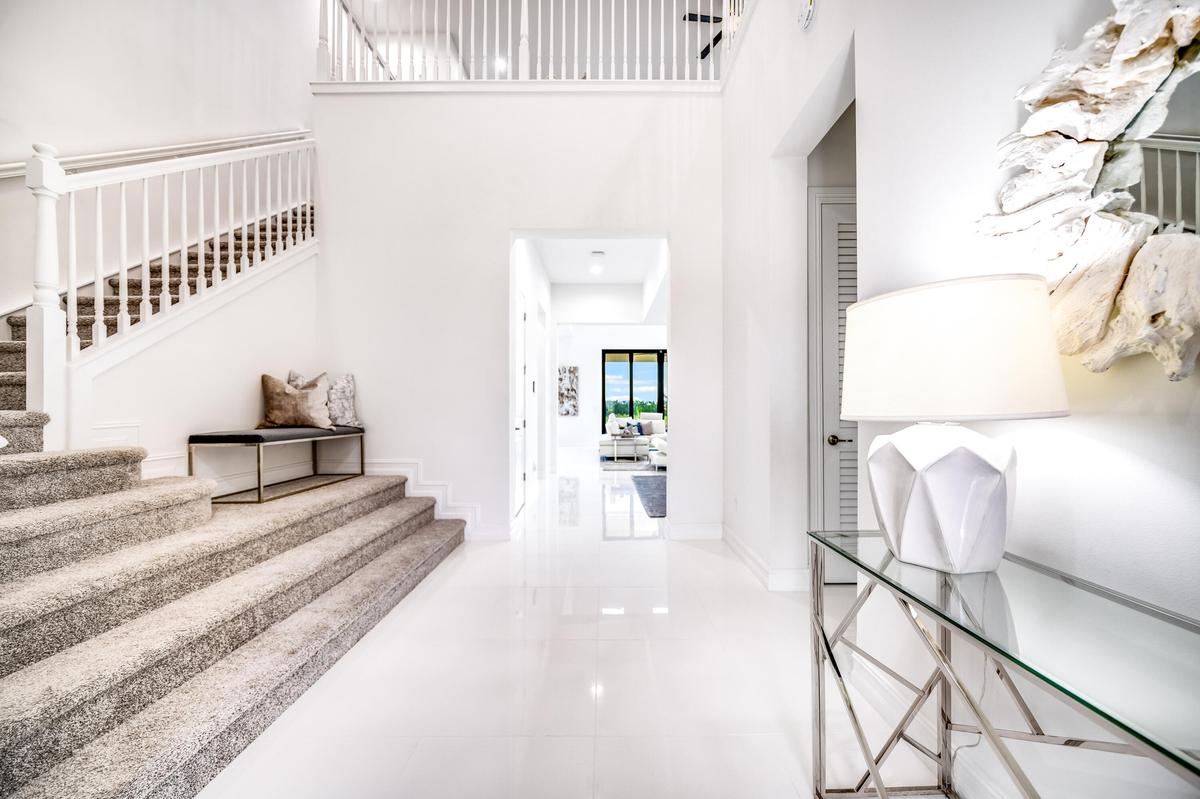 Two-story entry featuring white walls, a carpeted staircase with white balusters, and polished tile flooring