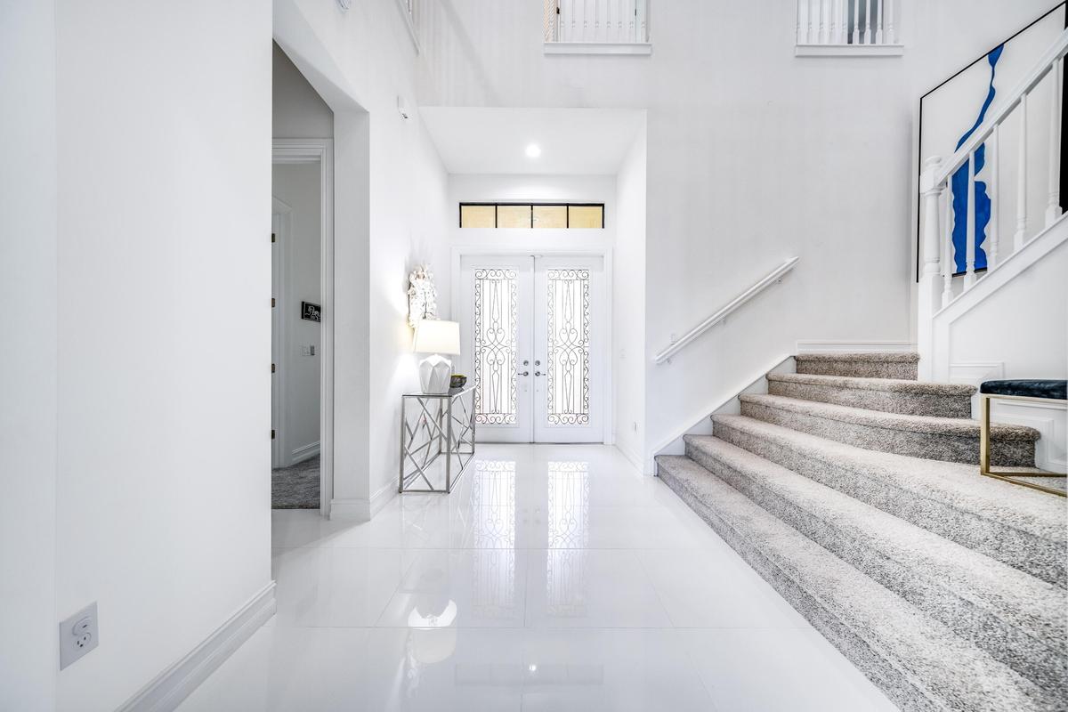 Double entry doors with decorative glass inserts, transom window, recessed lighting, polished tile flooring, and a carpeted staircase with white raili