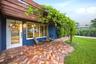 Wood pergola with lush greenery over a brick paver patio, featuring a full-light entry door and multiple windows