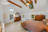 Spacious primary bedroom with vaulted ceiling, exposed wood beams, skylights, and abundant natural light