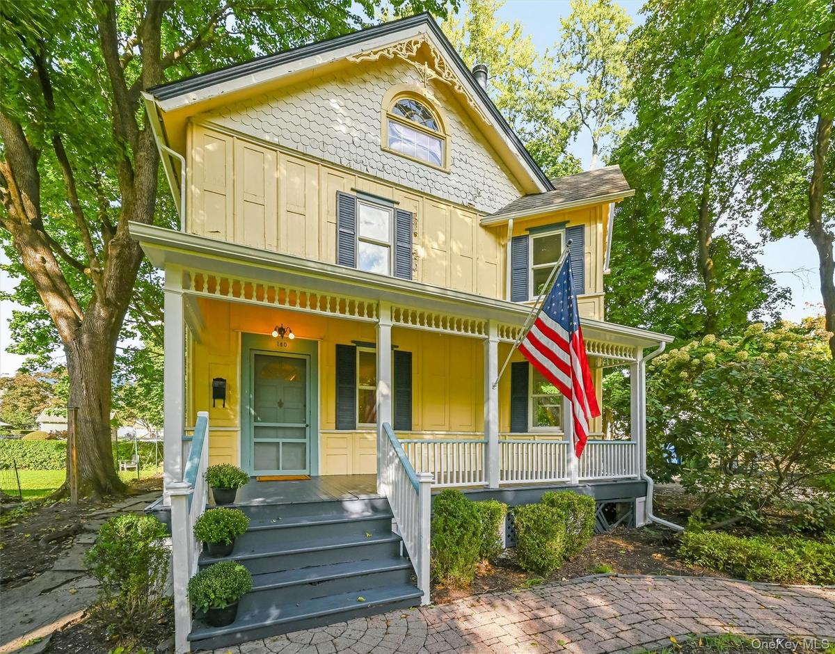 Victorian-style exterior with yellow siding, covered front porch, decorative gable trim, and a brick paver walkway