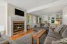 Fireplace with a white mantle and brick surround, hardwood flooring, built-in shelving, and white trim work