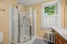 Corner shower enclosure with glass panels, white window shutters, and a wood-finish vanity with an integrated sink