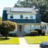 Gambrel roofline with solar panels, white siding, brick chimney, covered entry, and bay window