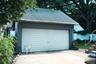 Detached  remote opening garage with a double vehicle door, asphalt shingle roof, and concrete driveway