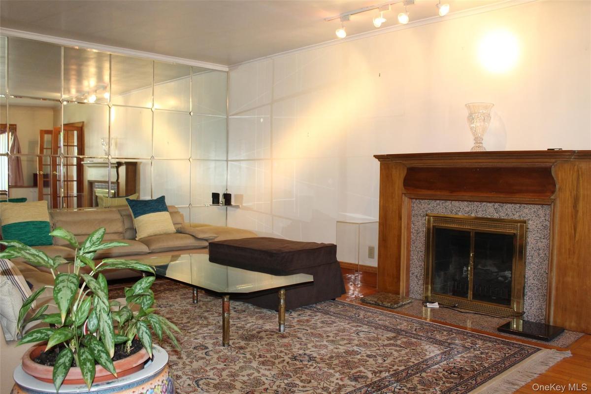 Living room has wood-finish flooring with a  working fireplace featuring a wood mantel and stone surround, and a wall of mirrored panels