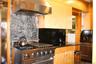 Stainless steel range with a professional-grade hood, natural wood-finish cabinetry, black stone countertops, and a tiled stone backsplash