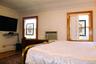 Large bedroom 1 with wood-frame windows with stained glass decorative inserts, white textured walls, and a wall-mounted air conditioning unit