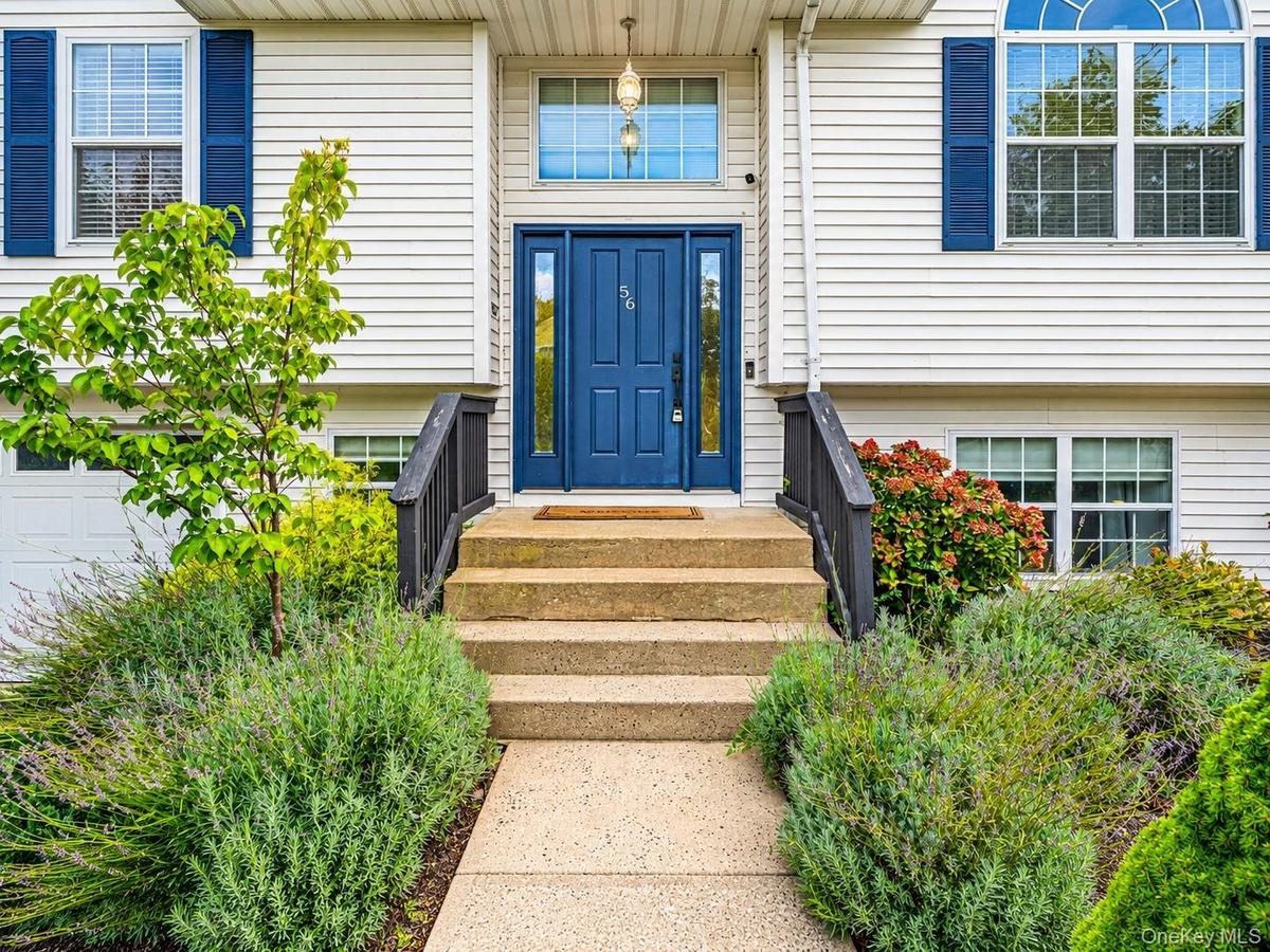 White siding exterior with a prominent blue entry door, complementary blue window shutters, an arched transom window, and a concrete pathway leading t
