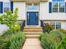 White siding exterior with a prominent blue entry door, complementary blue window shutters, an arched transom window, and a concrete pathway leading t