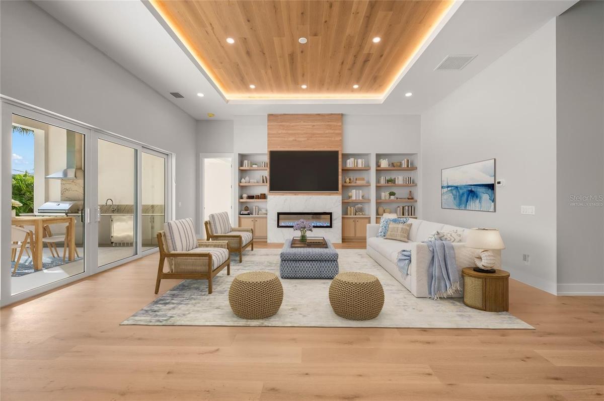 Virtually staged family room featuring a modern fireplace and custom built-ins, opening seamlessly to the outdoor entertaining area.