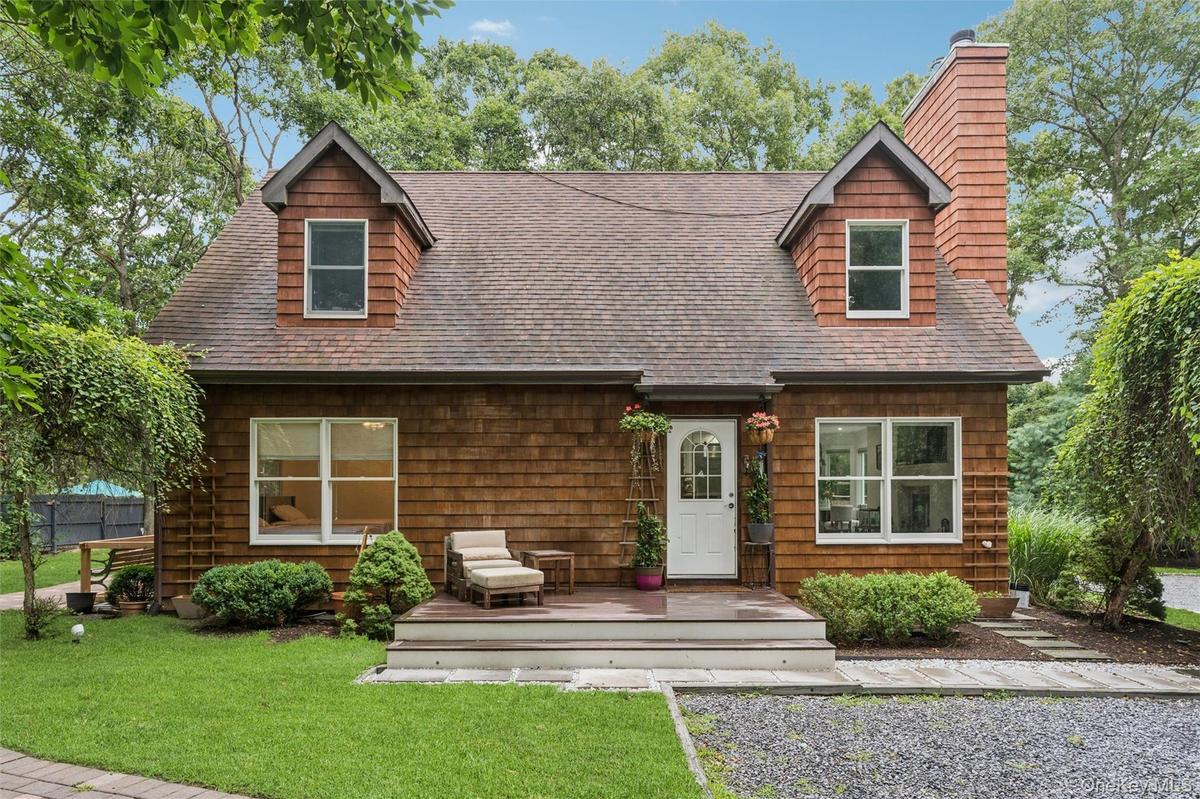Cedar shake siding, dormer windows, a prominent brick chimney, a front deck, and mature landscaping