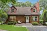 Cedar shake siding, dormer windows, a prominent brick chimney, a front deck, and mature landscaping