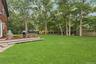 Expansive green lawn with mature trees, a multi-level wood-finish deck, and wood siding on the exterior