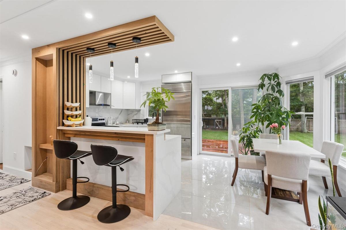 Modern kitchen featuring white cabinetry, stainless steel appliances, a breakfast bar with pendant lighting, a sliding glass door, and a dining area w