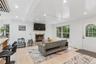 Vaulted ceiling with exposed beams, recessed lighting, wood-finish flooring, stone fireplace, and a white paneled entry door with an arched window