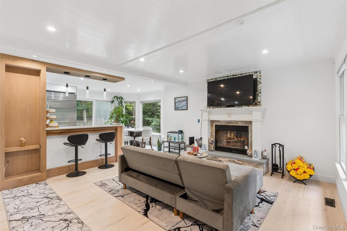 Open-concept living area featuring a stone-clad fireplace, light wood-finish flooring, recessed lighting, and a white shiplap ceiling