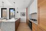 Kitchen with a peninsula, light wood finished floors, white cabinetry, hanging light fixtures, and black oven