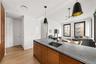 Kitchen with brown cabinetry, dark stone counters, hanging light fixtures, open floor plan, and modern cabinets