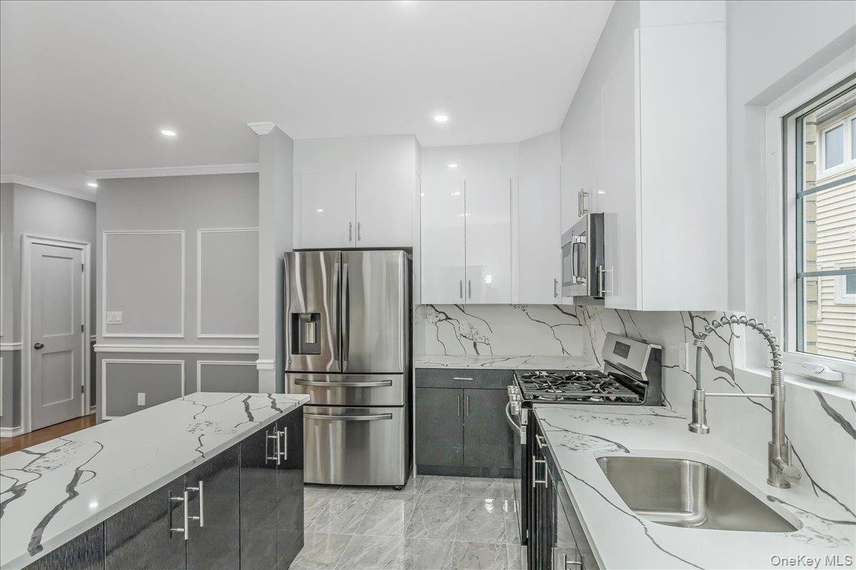 Kitchen with appliances with stainless steel finishes, white cabinets, modern cabinets, light stone countertops, and dark cabinetry