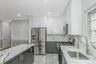 Kitchen with appliances with stainless steel finishes, white cabinets, modern cabinets, light stone countertops, and dark cabinetry