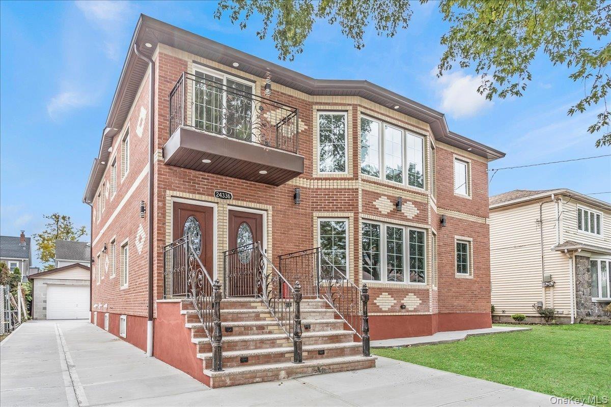 View of front of house with an outdoor structure, brick siding, a garage, a balcony, and a front yard