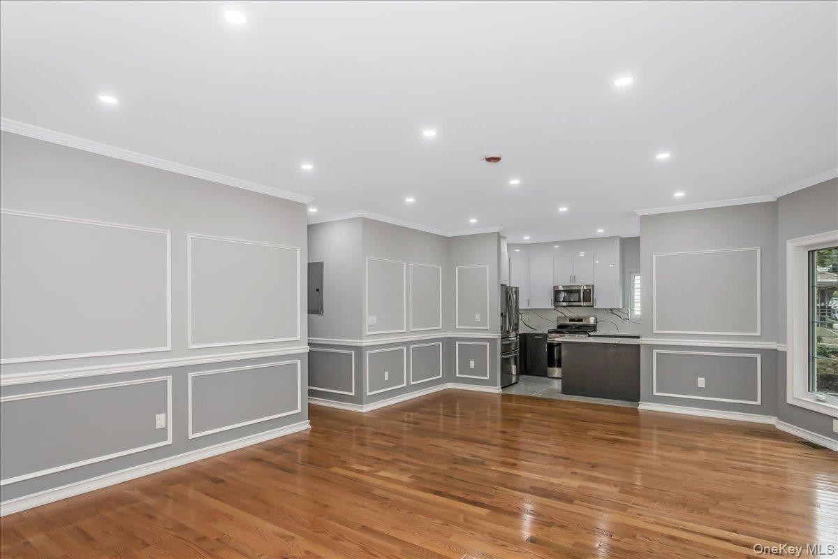 Unfurnished living room with a decorative wall, crown molding, light wood-style flooring, and recessed lighting