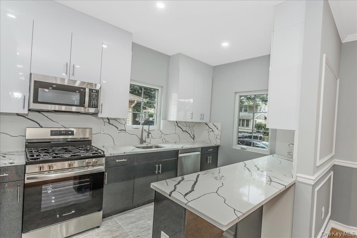 Kitchen featuring stainless steel appliances, light stone countertops, white cabinets, backsplash, and recessed lighting