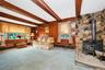 Wood paneling, exposed ceiling beams, stone accent wall, and a built-in wood-burning stove with a stone hearth