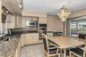 Kitchen featuring light-toned cabinetry, granite-finish countertops, stainless steel appliances, a tile backsplash, and a contemporary chandelier