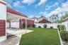 Expansive backyard featuring a manicured lawn, white picket fencing, and mature shrubbery