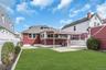 Manicured lawn, mature shrubs, white picket fence, covered patio, and red siding