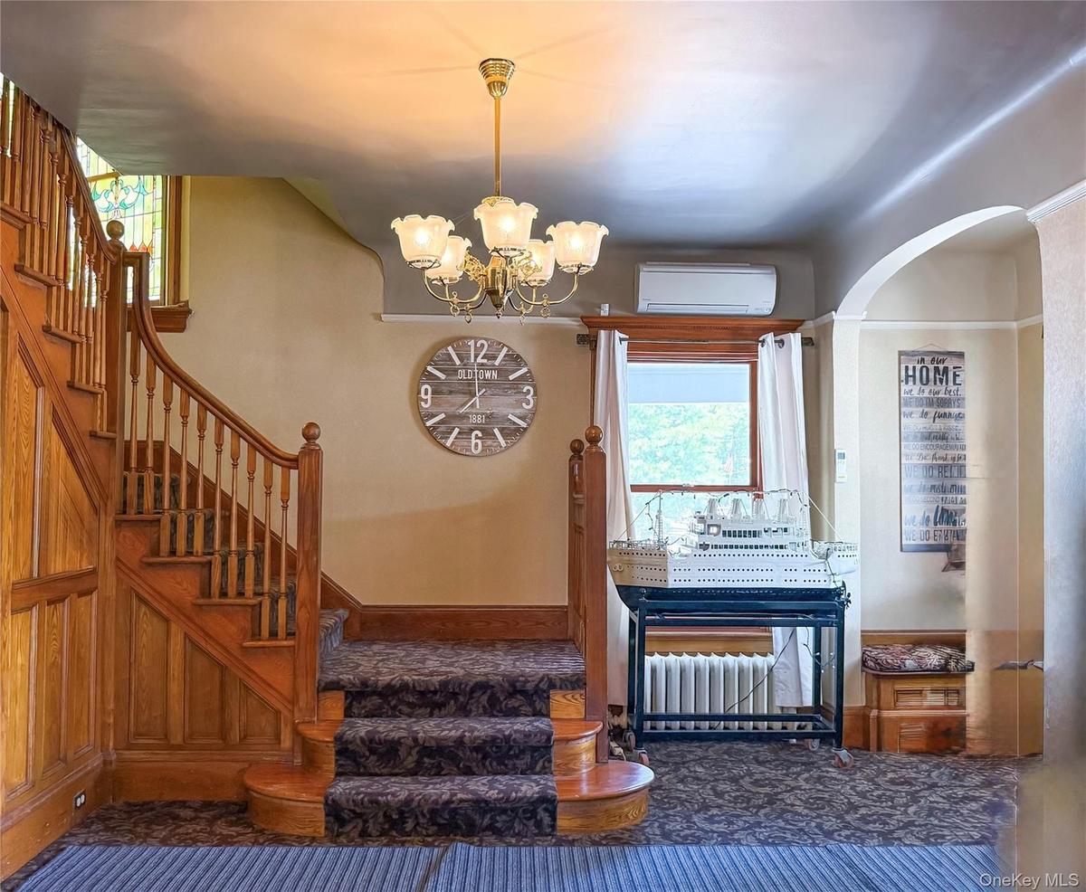 Grand Wood Staircase with carpeted and wood paneling, featuring a decorative chandelier and an arched doorway