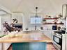Cottage kitchen featuring a central island with a wood countertop, white shaker cabinetry, stainless steel appliances, and open wood shelving