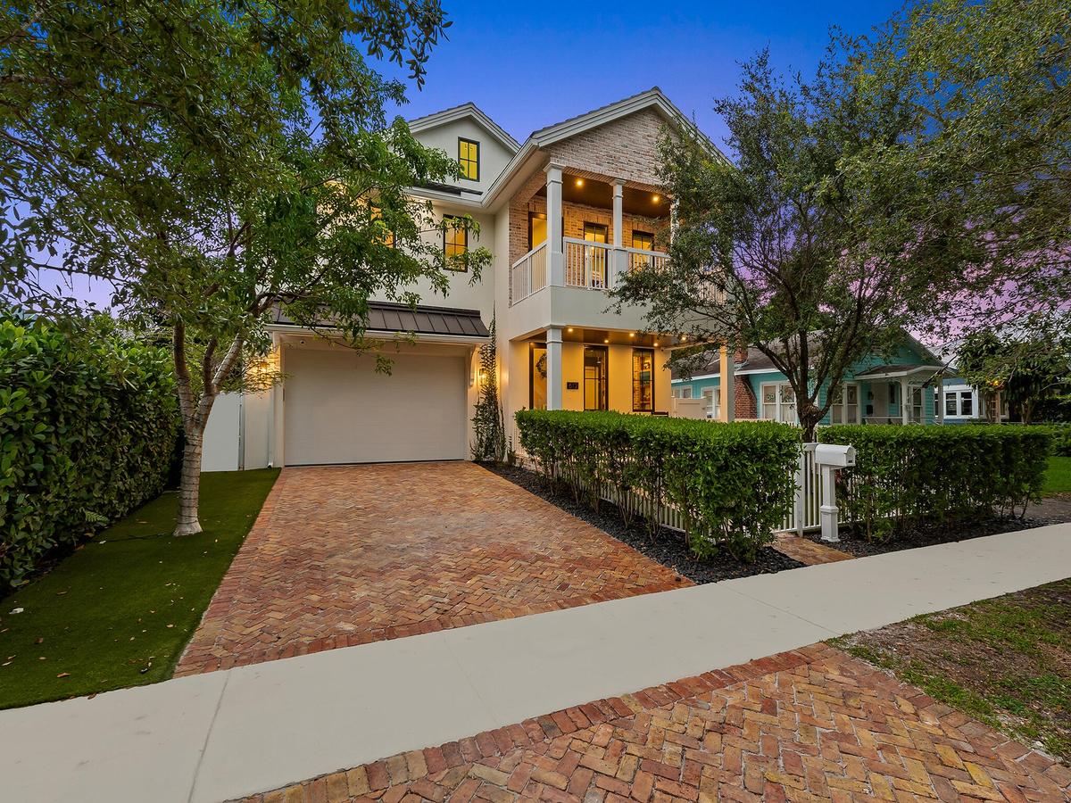 Front exterior at dusk with brick driveway and mature trees
