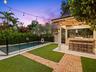 Backyard at dusk with pool, turf and lit pergola
