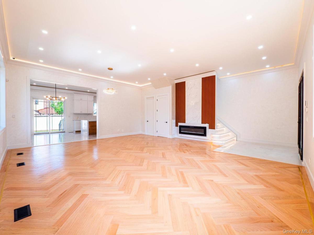 Herringbone wood-finish flooring, linear electric fireplace with marble-look and wood-look surround, recessed lighting, crown molding, and a built-in 