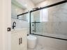 Full-height marbled tile, sleek black-framed shower enclosure, white vanity with textured cabinet doors, contemporary black faucet, and modern toilet